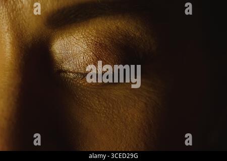 Ein Nahbild einer Frau mit geschlossenem Auge, das die zarte Textur ihrer Haut und Wimpern unter sanfter Umgebungsbeleuchtung hervorhebt. Das Bild spiegelt tr wider Stockfoto