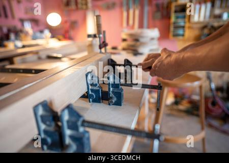Der Handwerker sichert verklebte Holzklötze mit Klemmen, um dicke Bretter zu bilden. Klebeschicht für Träger vorbereiten Stockfoto