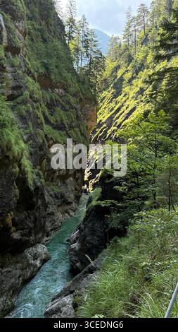 Eine malerische Schlucht mit einem Fluss, der sich durch üppiges Grün und steile felsige Klippen schlängelt. Sonnenlicht filtert durch hohe Bäume und wirft Schatten auf die Cany Stockfoto
