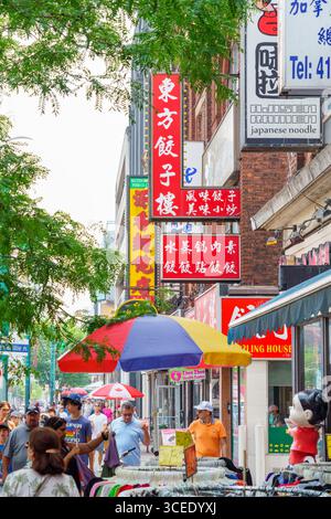 Die Leute laufen vorbei an Geschäften in Chinatown mit roten chinesischen Schildern und farbenfrohen Sonnenschirmen über Straßenverkäufern. Stockfoto