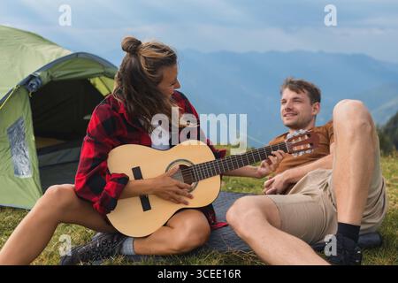 Junge Paare campen in den Bergen, spielen Gitarre, genießen Freiheit und verbinden sich mit der atemberaubenden Natur. Stockfoto