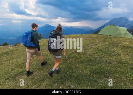 Junge Paare mit Rucksäcken, wandern in der Abenddämmerung bergauf in die Berge, erleben Abenteuer in der freien Natur. Stockfoto