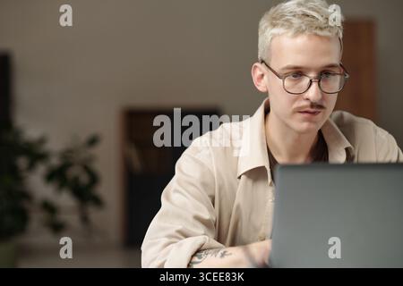 Junger Z-Mann mit Brille, der im modernen Büro am Laptop arbeitet, Kopierraum Stockfoto