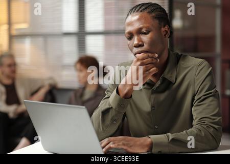 Nachdenklicher junger afroamerikanischer Manager, der auf Laptop-Bildschirm schaut, mittleres Porträt Stockfoto