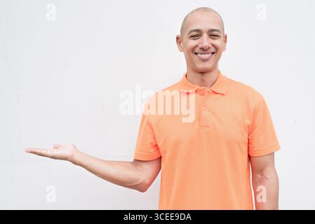 Studio-Porträt eines gutaussehenden mittelalten hispanischen Mannes im orangefarbenen Poloshirt vor weißem Hintergrund. Legere Lifestyle- und Modeschmuck Stockfoto