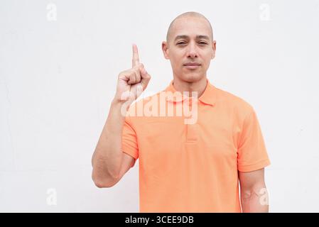 Studio-Porträt eines gutaussehenden mittelalten hispanischen Mannes im orangefarbenen Poloshirt vor weißem Hintergrund. Legere Lifestyle- und Modeschmuck Stockfoto