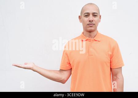 Studio-Porträt eines gutaussehenden mittelalten hispanischen Mannes im orangefarbenen Poloshirt vor weißem Hintergrund. Legere Lifestyle- und Modeschmuck Stockfoto