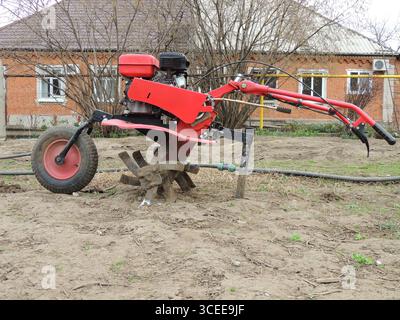 Roter Motorpflug, Seitenansicht, stehend auf trockenem Feldboden vor Backsteinhaus-Hintergrund Stockfoto