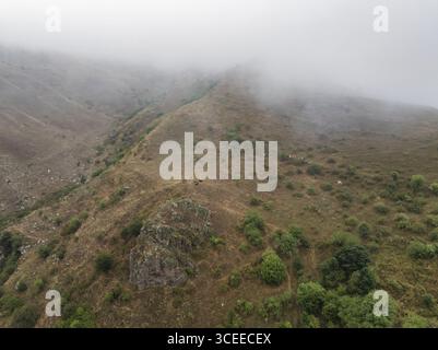 Blick aus der Vogelperspektive auf die von Nebel gehüllten Hügel mit karger Vegetation und felsigen Ausbissen, Old Goris, Provinz Syunik, Armenien. Stockfoto