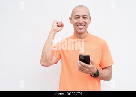 Studio-Porträt eines gutaussehenden mittelalten hispanischen Mannes im orangefarbenen Poloshirt vor weißem Hintergrund. Legere Lifestyle- und Modeschmuck Stockfoto