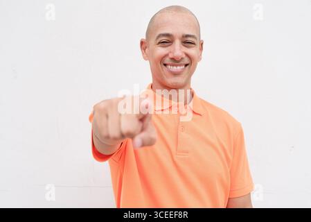 Studio-Porträt eines gutaussehenden mittelalten hispanischen Mannes im orangefarbenen Poloshirt vor weißem Hintergrund. Legere Lifestyle- und Modeschmuck Stockfoto