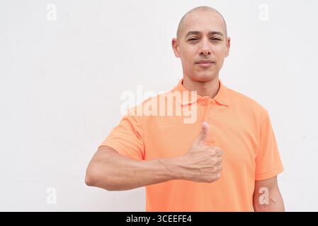 Studio-Porträt eines gutaussehenden mittelalten hispanischen Mannes im orangefarbenen Poloshirt vor weißem Hintergrund. Legere Lifestyle- und Modeschmuck Stockfoto