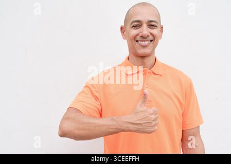 Studio-Porträt eines gutaussehenden mittelalten hispanischen Mannes im orangefarbenen Poloshirt vor weißem Hintergrund. Legere Lifestyle- und Modeschmuck Stockfoto