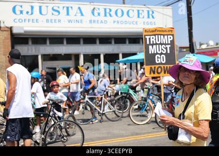 Venedig, Kalifornien, USA. August 2025. Eine Frau hält ein Anti-Trump-Schild, während die Teilnehmer am 61 Sonntag, den 18. August 2025, in Venedig an Gjusta Grocer auf der Windward Avenue vorbeifahren. Die Strecke erstreckte sich vom La Cienega Boulevard bis zum Venice Beach Boardwalk. (Credit Image: © Jonathan Alcorn/ZUMA Press Wire) NUR REDAKTIONELLE VERWENDUNG! Nicht für kommerzielle ZWECKE! Quelle: ZUMA Press, Inc./Alamy Live News Stockfoto