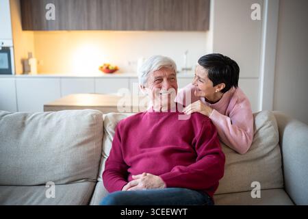 Glückliches älteres Paar, das zusammen auf dem Sofa sitzt und zu Hause lacht und redet. Ältere Familienliebe Stockfoto