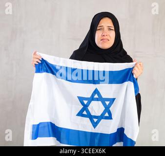 Eine aufgebrachte muslimische Frau im traditionellen schwarzen Hidschab hält die Flagge Israels Stockfoto