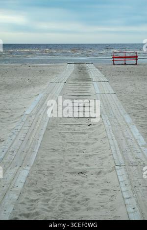Holzsteg führt vom Sandstrand zum Meer unter bewölktem Himmel. Strand von Pärnu Stockfoto