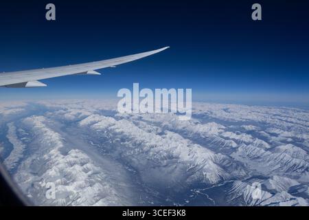 Aus der Vogelperspektive auf die schneebedeckten felsigen Berge der westlichen kanadischen Bergkette mit Flugzeugflügel und blauem Himmelsraum Stockfoto