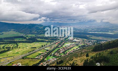 Atemberaubende Luftlandschaft des Jaime Duque Parks in Briceño, Cundinamarca, mit üppigen grünen Hügeln und Wohngebieten mit bewölktem Himmel. Stockfoto