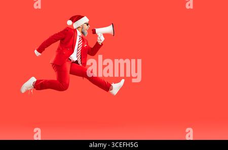 Alter Mann im Weihnachtsmann-Stil, Weihnachtsmütze springt schnell herauf schreienden Lautsprecher in der Luft auf rotem Hintergrund. Stockfoto