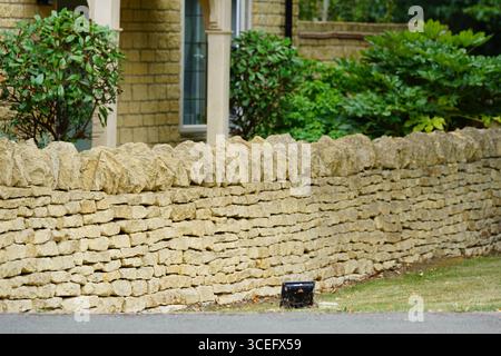 Traditionelle Steinmauer im ländlichen Garten mit Grün und Büschen im Hintergrund. Chipping Norton, England Stockfoto