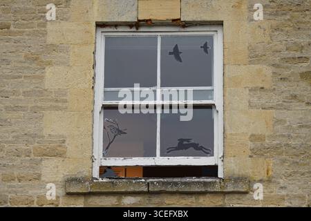Altes rustikales Fenster mit Tiersilhouetten und Backsteinmauern. Chipping Norton, England Stockfoto