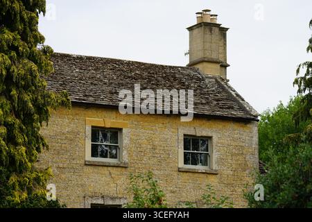 Rustikales Steinhaus mit gekacheltem Dach umgeben von üppigem Grün. Bourton-on-the-Water, England Stockfoto