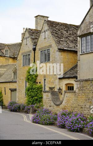Traditionelle Steinhäuser gesäumt von lebhaften Blumen in einem malerischen Dorf. Bourton-on-the-Water, England Stockfoto