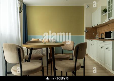 Das Innere eines kleinen Apartments mit Bett, Kissen, hellen Küchenmöbeln, Stühlen mit Tisch, Küchengeräten und Kühlschrank. Das Apartment hat Stockfoto
