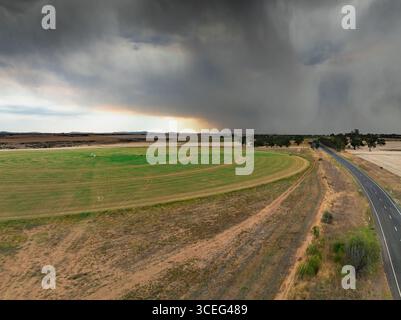 Aus der Vogelperspektive fällt Regen aus dunklen Sturmwolken über einem grünen kreisförmigen Feld auf dem Ackerland am Joyces Creek in Central Victoria, Australien. Stockfoto