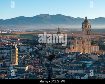 Die goldene Fassade und die komplizierten Türme der Kathedrale von Segovia ragen majestätisch über die historische Stadt, eingerahmt von fernen Bergen, Segovia, Castilla y León, Spanien. Stockfoto