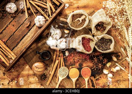 Blick von oben auf kulinarische Gewürze und Kräuter, heiße rote Chili, weißen Pfeffer, getrocknetes Chilipulver in Löffeln, Knoblauch, Gewürze in Säcken, Zimt, Weizen auf Woo Stockfoto