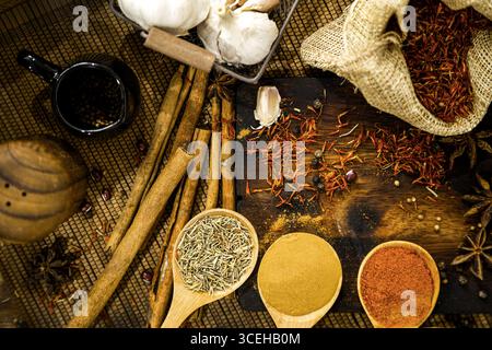 Blick von oben auf kulinarische Gewürze und Kräuter, heiße rote Chili, weißen Pfeffer, getrocknetes Chilipulver in Löffeln, Knoblauch, Gewürze in Säcken, Zimt, Weizen auf Woo Stockfoto