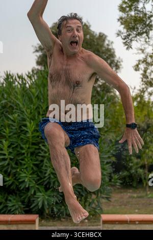 Ein nasser Mann im Badeanzug springt hoch in ein Schwimmbad Stockfoto