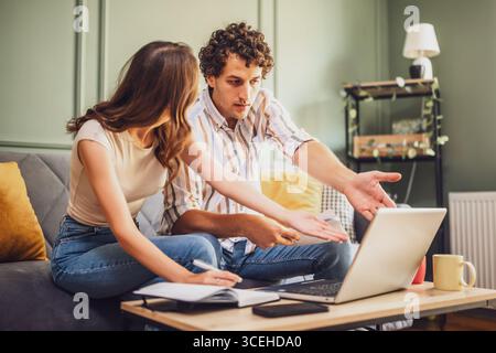 Ein Paar spricht über die Finanzierung von Wohnräumen auf einem Laptop und berechnet das Familienbudget im Wohnzimmer. Sie sind verzweifelt. Stockfoto