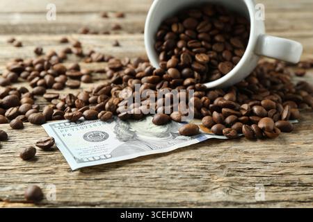 Dollarscheine, Kaffeebohnen und Tasse auf Holztisch, Nahaufnahme Stockfoto