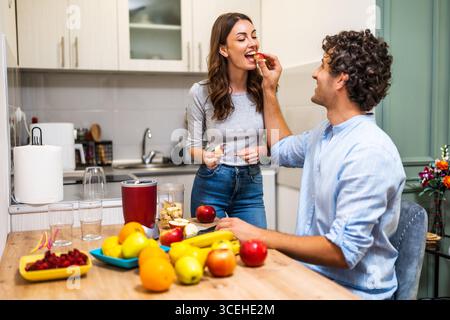 Ein erwachsenes Paar bereitet Smoothie in der Küche zu. Sie haben verschiedene Früchte, die in einem elektrischen Entsafter gemischt werden können. Stockfoto