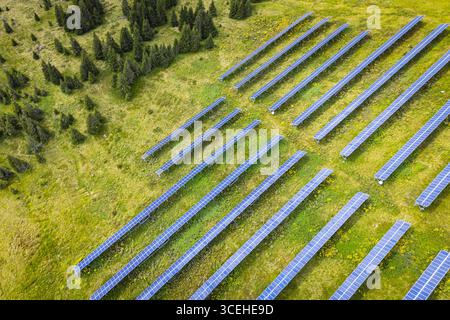 Aus der Vogelperspektive erstrahlen Solarpaneele unter der Sommersonne im Kontrast zu den saftig grünen Wiesen und dunklen immergrünen Wäldern im Lachtal, Steiermark, Österreich. Stockfoto