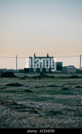 Ein kleines Haus mit Fenster ist auf einem Feld. Der Himmel ist blau und die Sonne untergeht Stockfoto