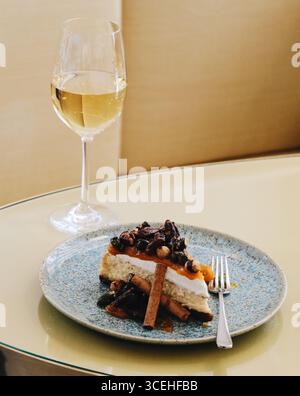 Dessert- und Getränkekombination, eine Scheibe gesalzenen Karamell-Käsekuchen mit karamellisierten Nüssen auf blauer Keramikplatte und Weißwein. Elegant Stockfoto