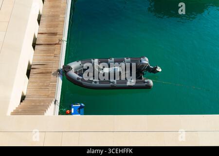 Blick von oben auf ein modernes graues, starres aufblasbares Motorboot, das an einem hölzernen Pier in klarem türkisfarbenem Meerwasser verankert ist. Stockfoto