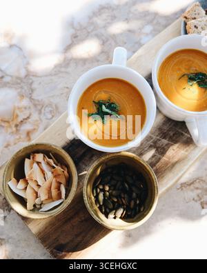 Blick von oben auf individuell servierte klassische Kürbissuppe, garniert mit Kräutern und Olivenöl und einer Seite mit gesunden nussigen Toppings. Essen im Freien Stockfoto