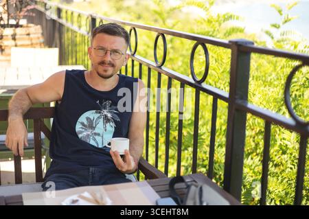 Junger Mann, der Kaffee auf einer Sommerterrasse genießt Stockfoto