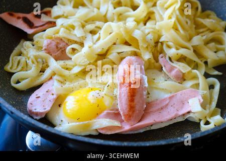 Die Pasta-Zubereitung in einer Pfanne, garniert mit Spiegelei und Würstchen, ergibt eine köstlich einfache Mahlzeit, die mit Gewürzen für eine angenehme Mischung aus gewürzt wird Stockfoto