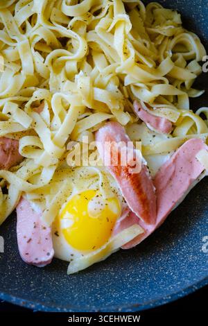 Nudeln mit aromatischen Kräutern und Gewürzen werden in einer Pfanne gekocht, zusammen mit herzhaften Würstchen und einem perfekt Spiegelei, was zu einer schnellen und köstlichen Mahlzeit führt Stockfoto