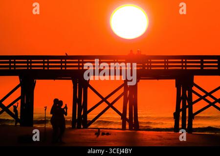 Isle Of Palms, Usa. Januar 2016. Menschen, die beim Sonnenaufgang über dem Atlantischen Ozean am Strand in der Nähe des Angelpiers am 18. August 2025 in Isle of Palms, South Carolina, eine Silhouette ziehen. Hohe Wellen und potenzieller Sturm serge wird später in der Woche erwartet, als Hurrikan Erin, ein Sturm der Kategorie 4, vor der Küste vorbeizieht. Quelle: Richard Ellis/Richard Ellis/Alamy Live News Stockfoto