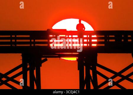 Isle Of Palms, Usa. Januar 2016. Ein Fischer, der beim Sonnenaufgang über dem Atlantik auf dem Front Beach Fishing Pier, 18. August 2025 in Isle of Palms, South Carolina, eine Silhouette bildet. Hohe Wellen und potenzieller Sturm serge wird später in der Woche erwartet, als Hurrikan Erin, ein Sturm der Kategorie 4, vor der Küste vorbeizieht. Quelle: Richard Ellis/Richard Ellis/Alamy Live News Stockfoto