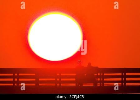 Isle Of Palms, Usa. Januar 2016. Ein Paar, das beim Sonnenaufgang über dem Atlantischen Ozean eine Silhouette bildet, beobachten Sie am Front Beach Fishing Pier, 18. August 2025 in Isle of Palms, South Carolina. Hohe Wellen und potenzieller Sturm serge wird später in der Woche erwartet, als Hurrikan Erin, ein Sturm der Kategorie 4, vor der Küste vorbeizieht. Quelle: Richard Ellis/Richard Ellis/Alamy Live News Stockfoto