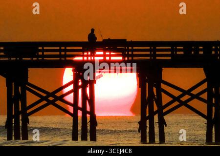 Isle Of Palms, Usa. Januar 2016. Ein Fischer, der beim Sonnenaufgang über dem Atlantik auf dem Front Beach Fishing Pier, 18. August 2025 in Isle of Palms, South Carolina, eine Silhouette bildet. Hohe Wellen und potenzieller Sturm serge wird später in der Woche erwartet, als Hurrikan Erin, ein Sturm der Kategorie 4, vor der Küste vorbeizieht. Quelle: Richard Ellis/Richard Ellis/Alamy Live News Stockfoto