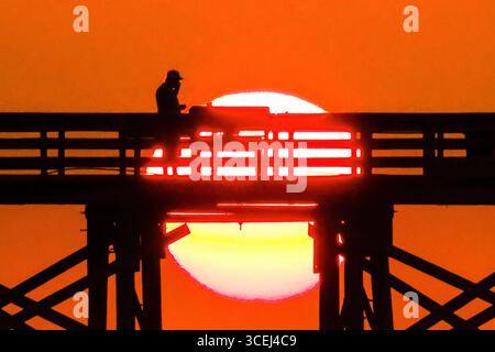 Isle Of Palms, Usa. Januar 2016. Ein Fischer, der beim Sonnenaufgang über dem Atlantik auf dem Front Beach Fishing Pier, 18. August 2025 in Isle of Palms, South Carolina, eine Silhouette bildet. Hohe Wellen und potenzieller Sturm serge wird später in der Woche erwartet, als Hurrikan Erin, ein Sturm der Kategorie 4, vor der Küste vorbeizieht. Quelle: Richard Ellis/Richard Ellis/Alamy Live News Stockfoto